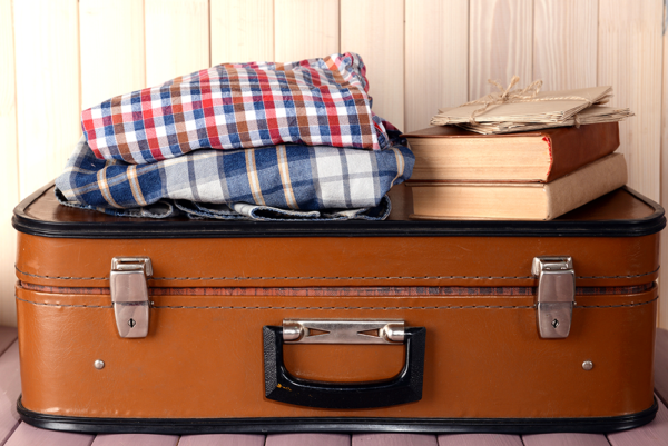 old fashion suitcase with men's clothes and books on top of it