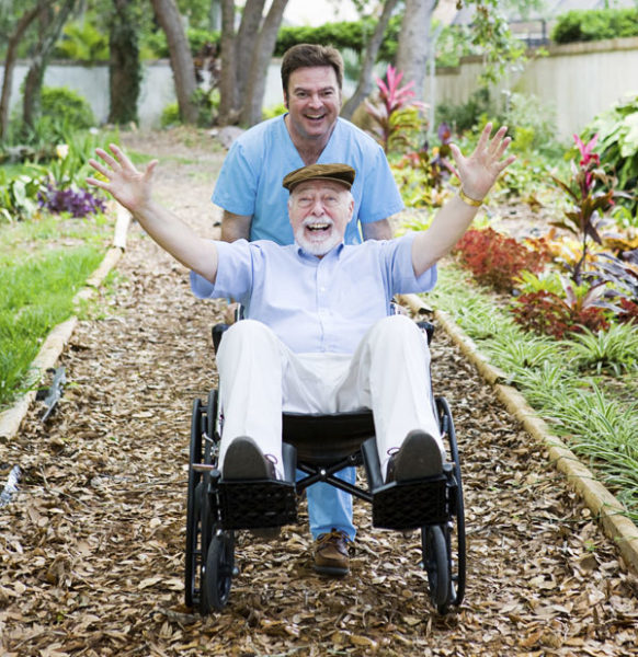young male caregiver pushing an elderly man in a wheelchair and doing a wheely