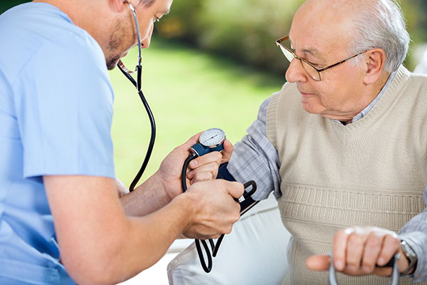 Male nurse checking blood pressure of senior man at nursing home