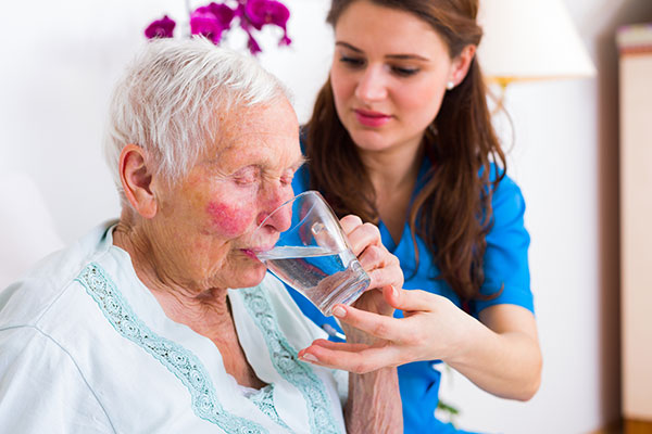 Kind caregiver bringing water to the thirsty sick elderly woman in bed.