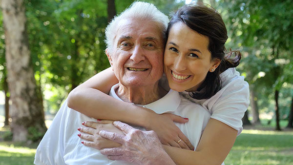 young female caregiver with her arms around elderly male resdient