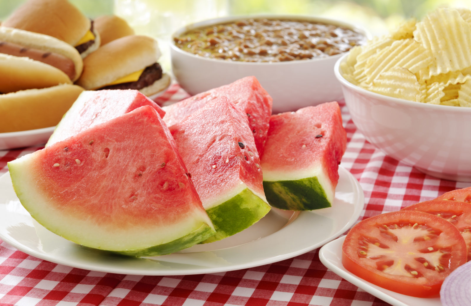 picnic table set with slices of watermelon and summer food favorites like chips and dip and hamburgers