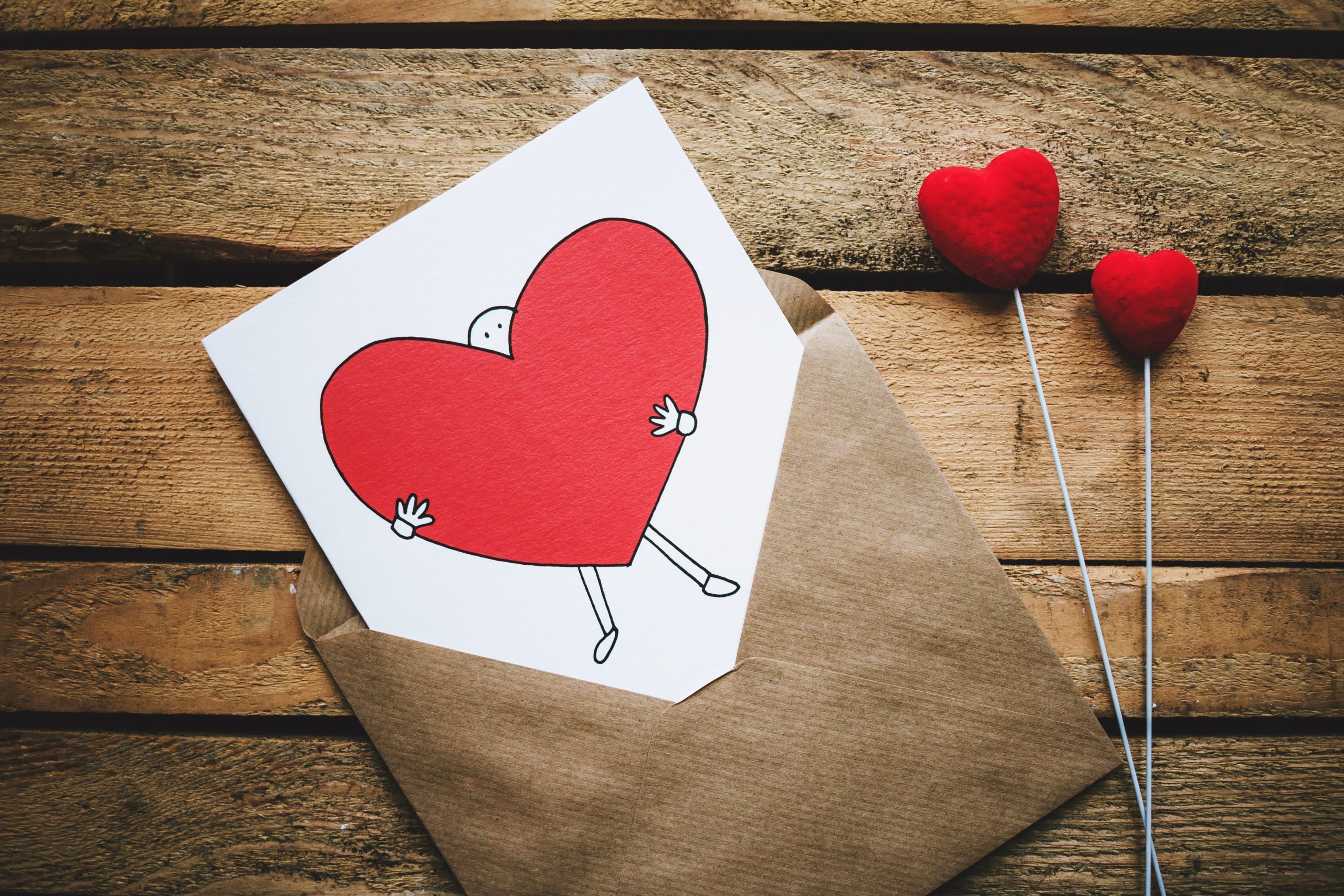 White card with red heart in a brown paper envelop sitting on a wood table