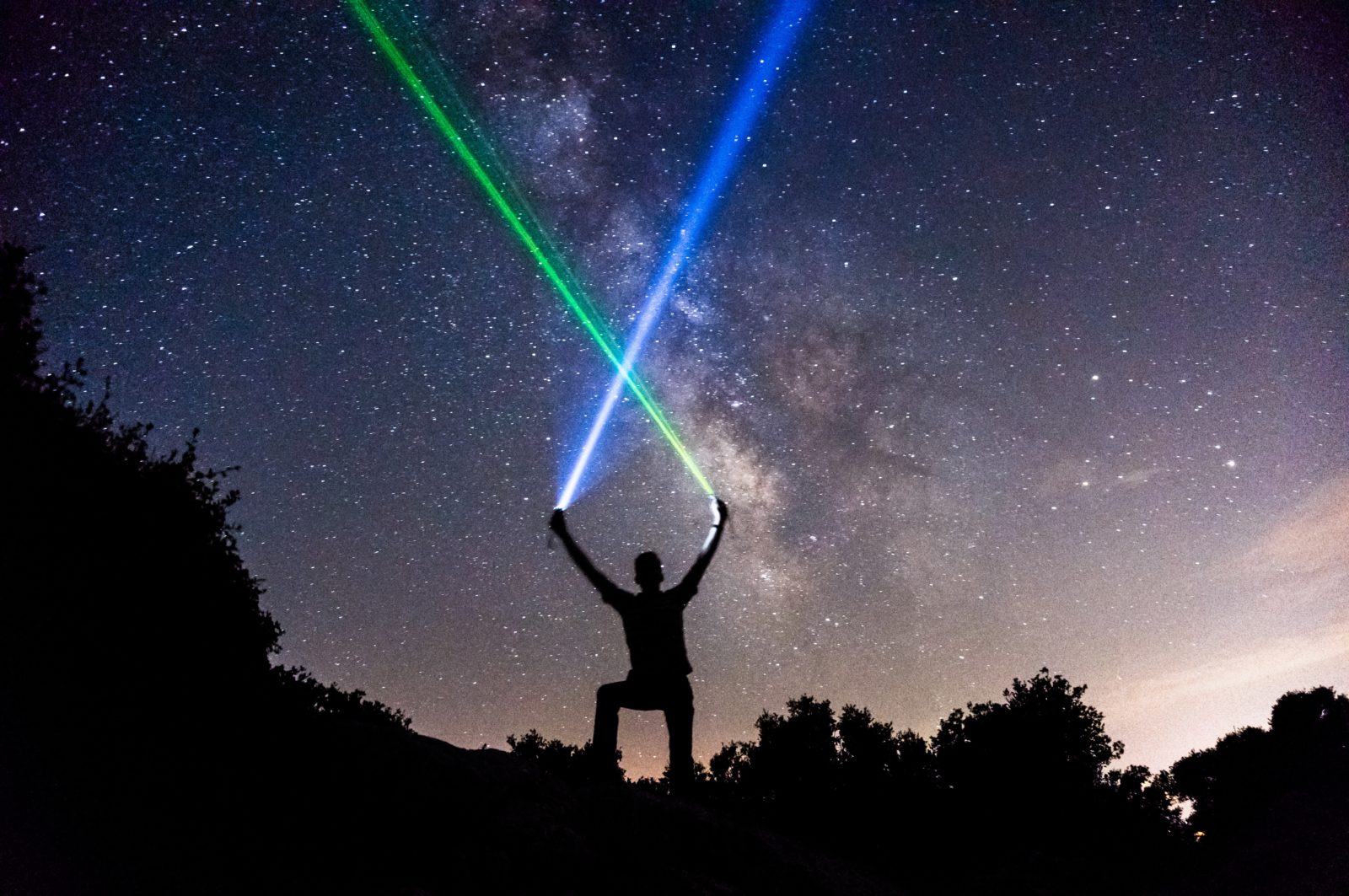 silhouette of man standing with dark sky behind him with hands raised and two light sabers