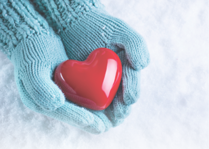 close up of hands wearing warm blue gloves holding a red heart shaped stone