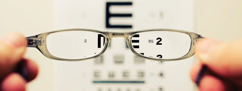 close up photo of person holding pair of glasses in front of eye chart