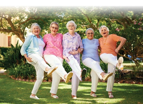 group of senior women kicking up their feet dancing in a line in the park