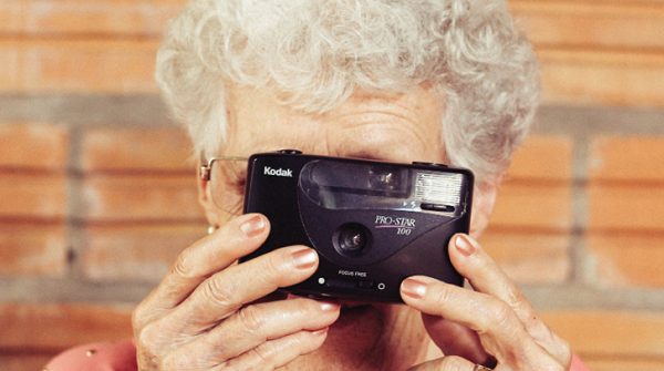 mature woman holding old style Kodak camera up to her eye to take a photo
