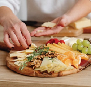close up of woman laying out cheese and fruit on wood tray