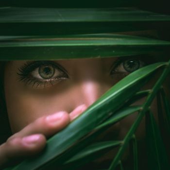 woman with dark green eyes peeking through dark green leaves