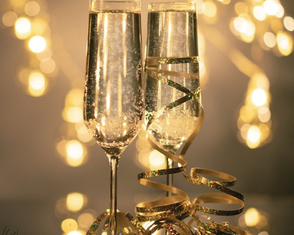 tall champagne flutes on table in foreground twinkling lights in background