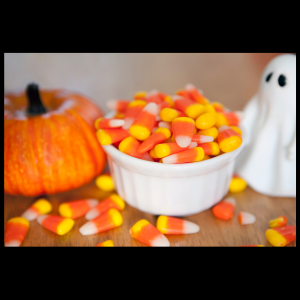 canva image of a bowl of candy corn candy with an orange pumpkin and ghost decoration